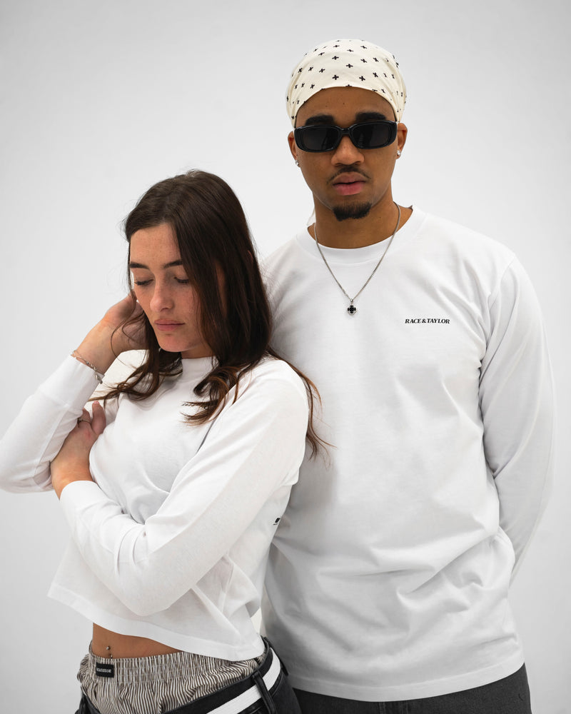 A male and a female model wearing long sleeve white skater T-shirts. The male model has his hand on the female model's shoulder, and both are looking off to the side.