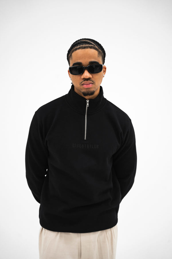 A person wearing a black quarter zip sweatshirt with the Race & Taylor brand embroidery on the front.